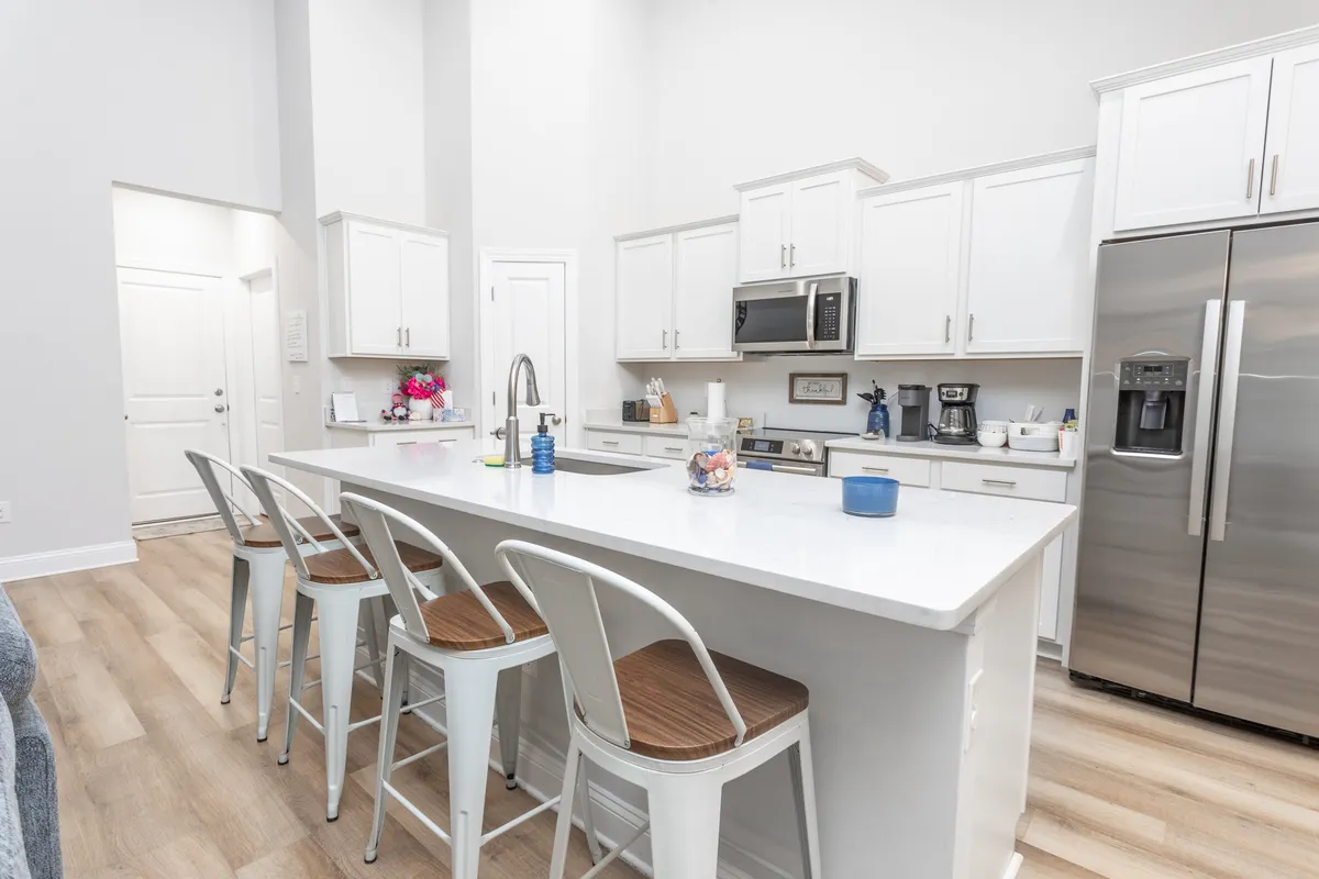 A contemporary kitchen with an inviting island countertop, stainless steel appliances, and several bar stools lined up. The open floor plan suggests a social, multi-cook environment ideal for both cooking and casual eating.