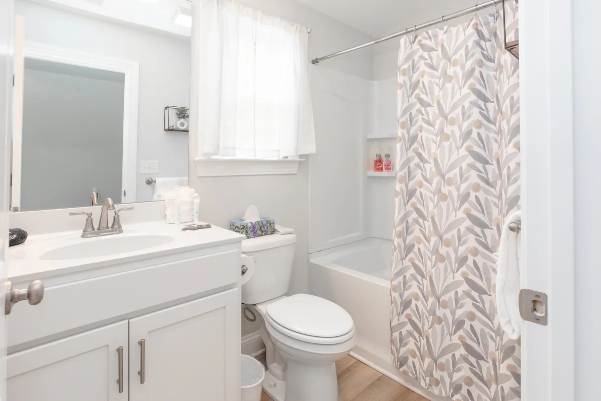A bright bathroom scene showcasing a vanity sink, bathtub, shower curtain, and toilet. The room is fresh and calming, ideal for both invigorating morning showers and relaxing bubble baths after a long day.