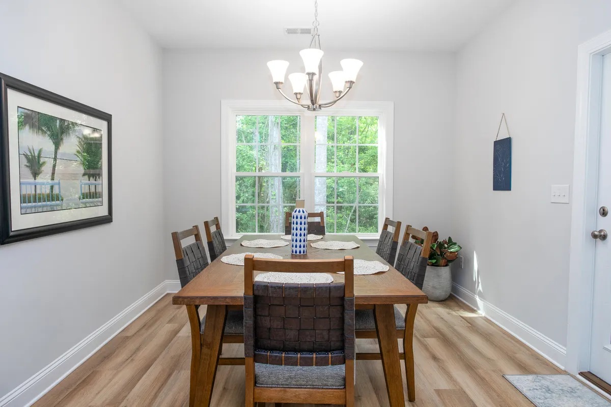 A warm, welcoming dining area featuring a generous dining table, elegant chandelier, and windows that let in glowing natural light. The setting is inviting and designed for group meals, celebrations, and family conversations.