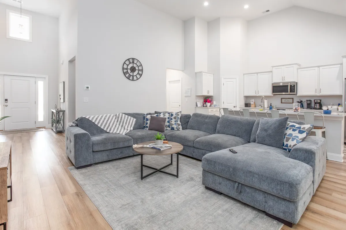 An inviting open-plan space that seamlessly blends a large sectional sofa, a central coffee table, and a visible kitchen area in the background. The overall layout facilitates easy movement and encourages group interaction, ideal for family gatherings and social occasions.