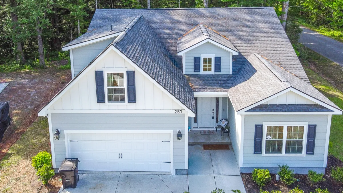 An inviting exterior view of the home's front porch, featuring shuttered windows, a garage door, and a beautifully landscaped garden. The welcoming porch suggests a restful retreat and a place to decompress after beach adventures.