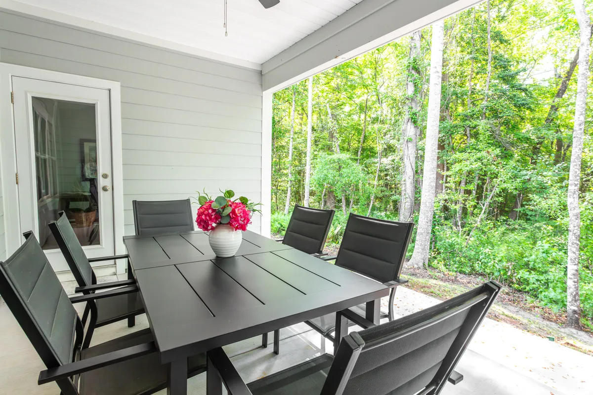 This exterior shot captures a tranquil outdoor dining area with a table set amidst a lush forest backdrop. The bright flower vase, sunlit table, and surrounding greenery convey a sense of relaxation and outdoor enjoyment just steps from home.