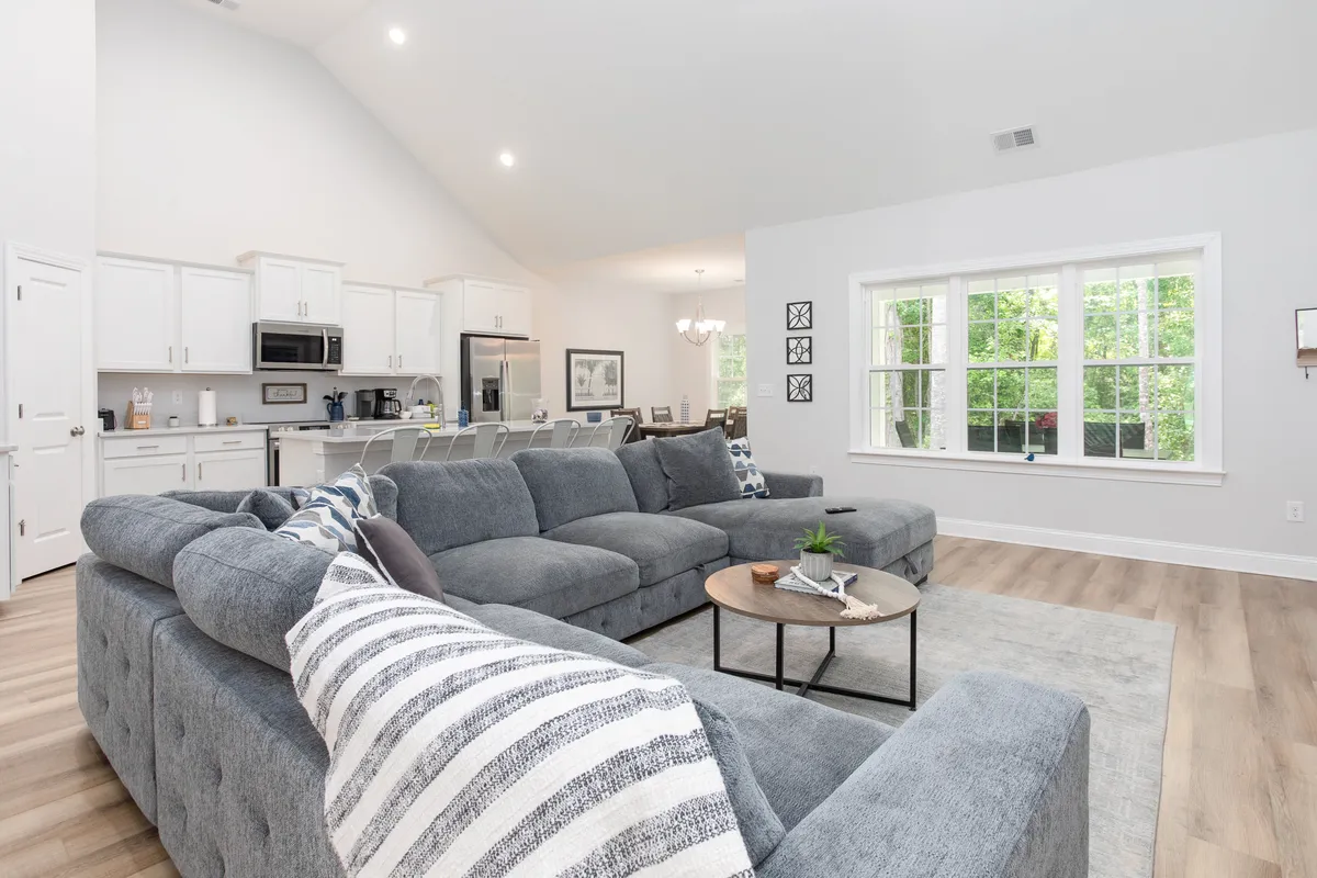 The spacious living area features a large sectional sofa, coffee table, and windows that let in abundant greenery. The space is arranged for relaxing with a group, celebrating, or enjoying quiet moments after a rewarding round of golf.